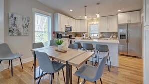 A modern kitchen with white cabinets, a central island, and a dining area with grey chairs.