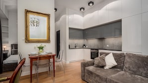 A modern living room with a grey sofa, a dining table with chairs, a large mirror, and a kitchen area with grey cabinets and a built-in oven. - Apartamenty Sun & Snow Przy Barbakanie (Warsaw)