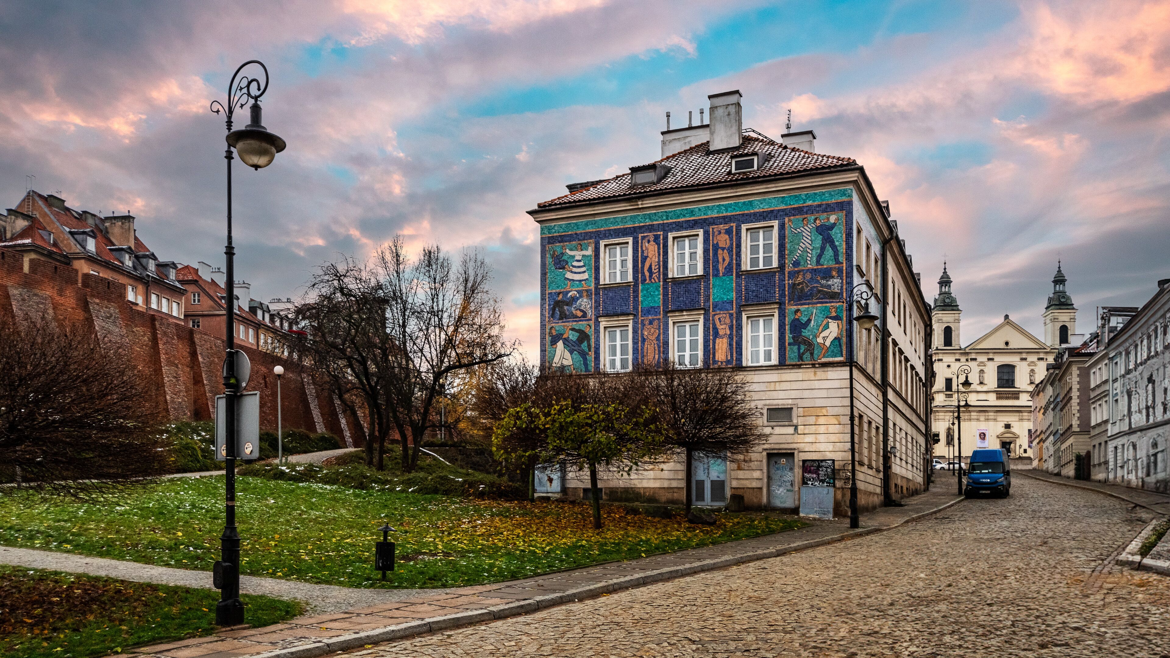 Eine Kopfsteinpflasterstraße gesäumt von historischen Gebäuden, eines davon mit einer farbenfrohen Mosaikfassade.