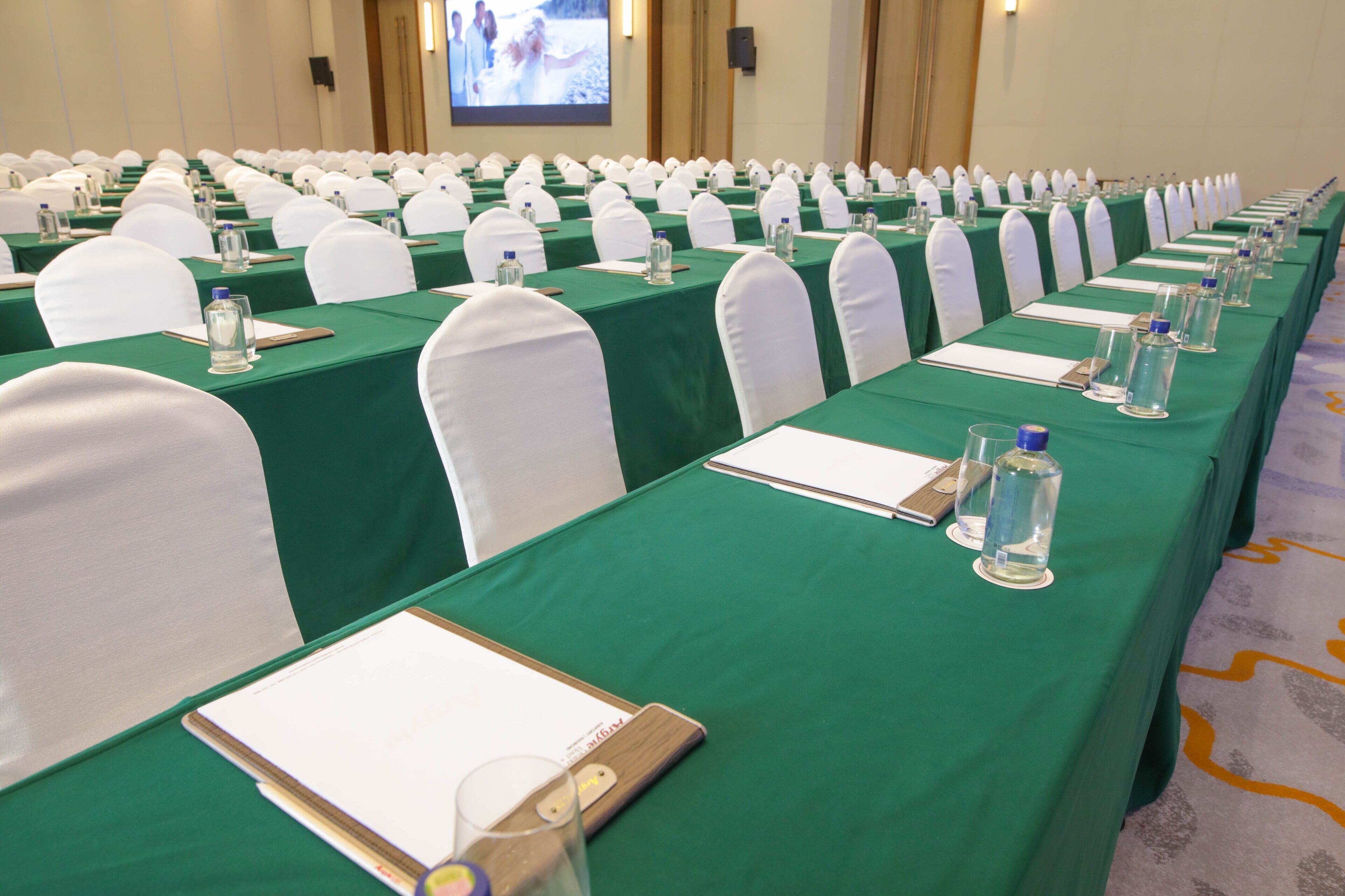 A conference room with rows of tables, each equipped with water bottles, notepads, and pens.