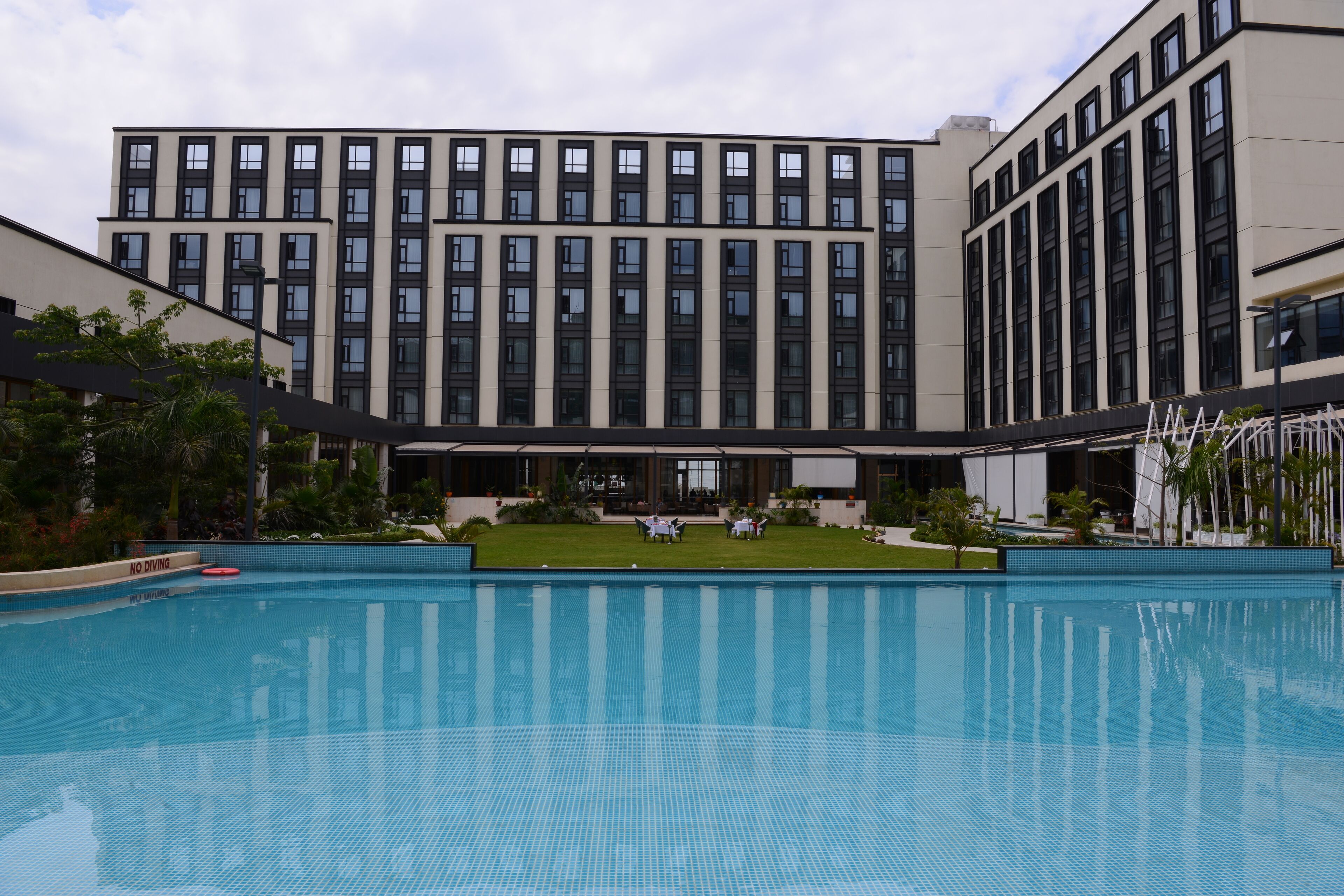 Ein modernes Hotel mit großzügigem Poolbereich, einem gepflegten Rasen und einem mehrstöckigen Gebäude mit einheitlicher Fassade.