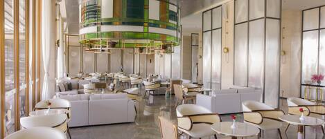 Un hall d’hôtel moderne doté d’un espace salon central, de plusieurs tables et d’un plafond au motif distinctif, aux couleurs vert et blanc.