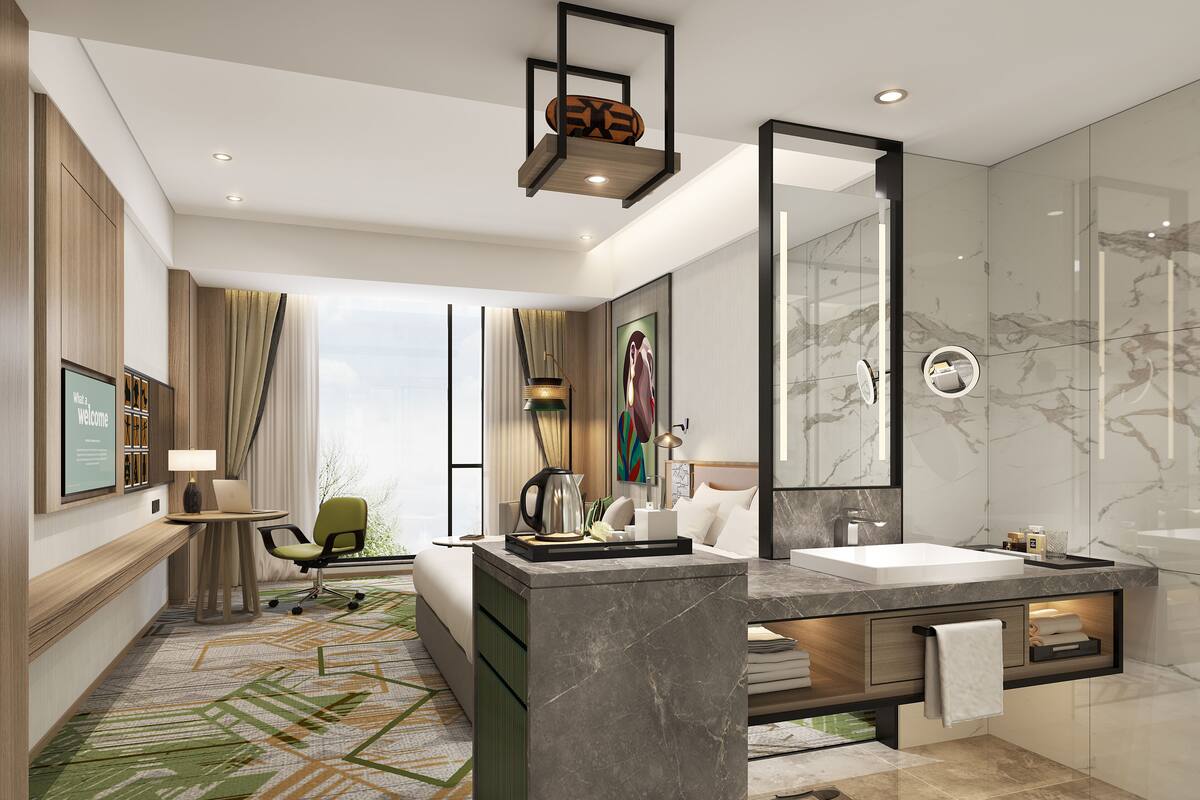 Une chambre d’hôtel moderne dotée d’un grand lit, d’un coin salon avec un bureau et une chaise, d’une grande salle de bain avec un lavabo et un miroir en marbre, et offrant une vue sur la ville grâce à de grandes fenêtres.