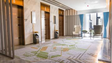 A modern hotel lobby with marble floors, elevators, a reception desk, and a seating area with a view.