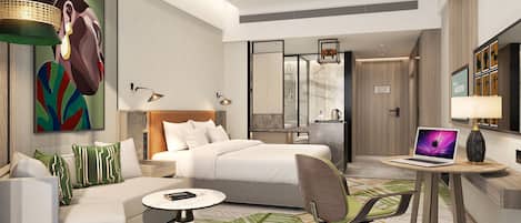 A modern hotel room with a bed, a sofa, a desk with a laptop, and a shower area.