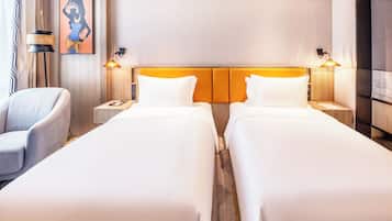 A hotel room with two single beds, a chair, a nightstand with a lamp, and a wall-mounted artwork.