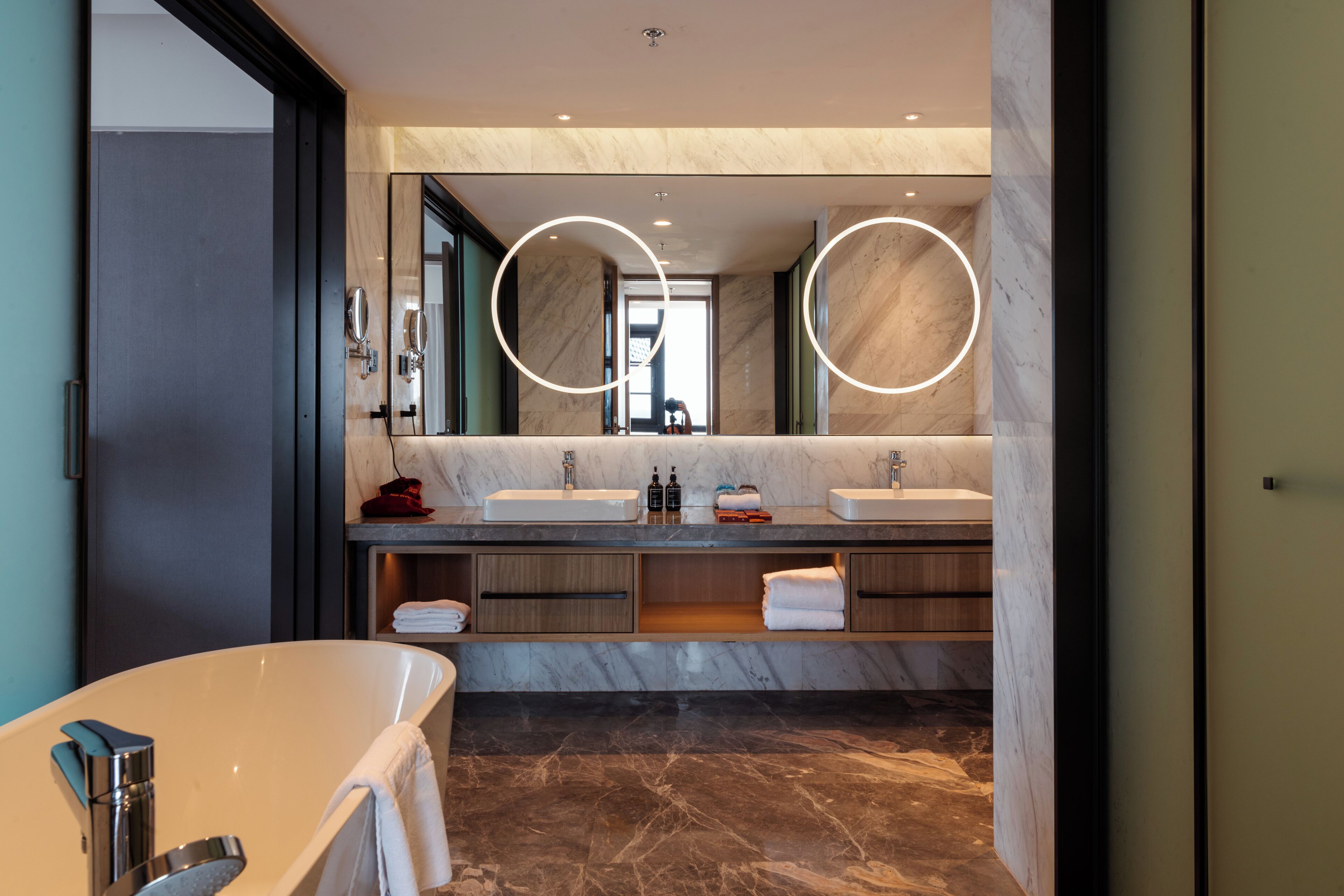 A modern bathroom with two sinks, a large mirror, and a bathtub.