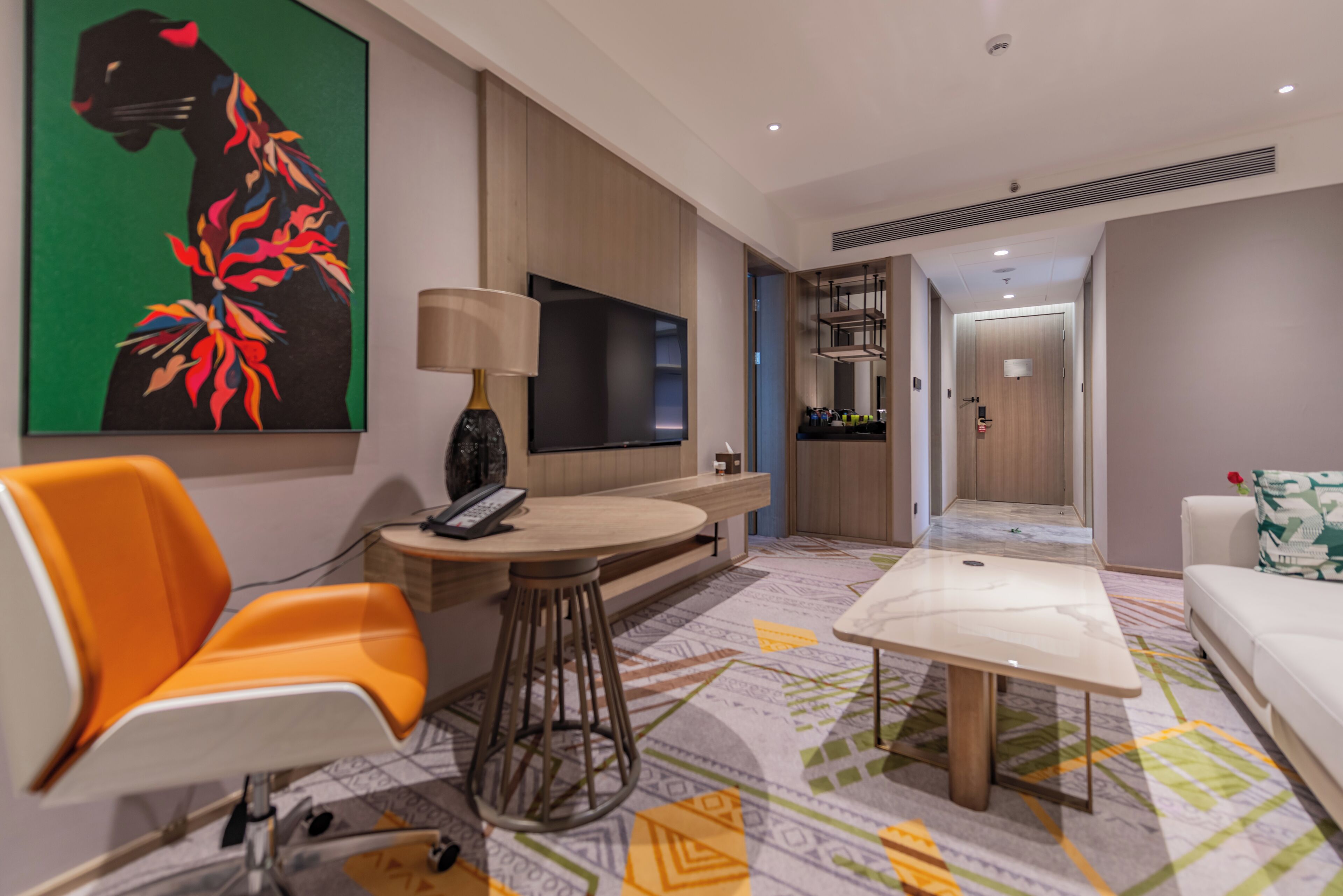 A modern hotel room with a sofa, a dining table, a TV, and a painting on the wall.