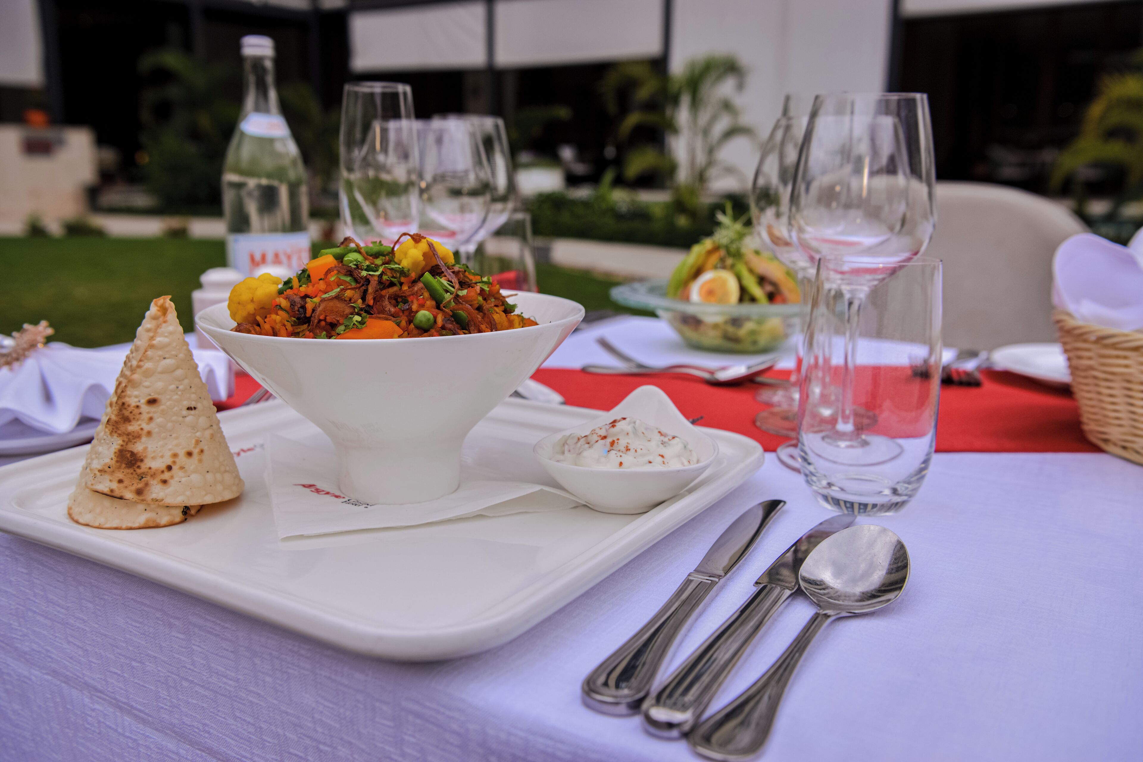 A dining table with a white plate, a bowl of food, a bottle of wine, and empty wine glasses.