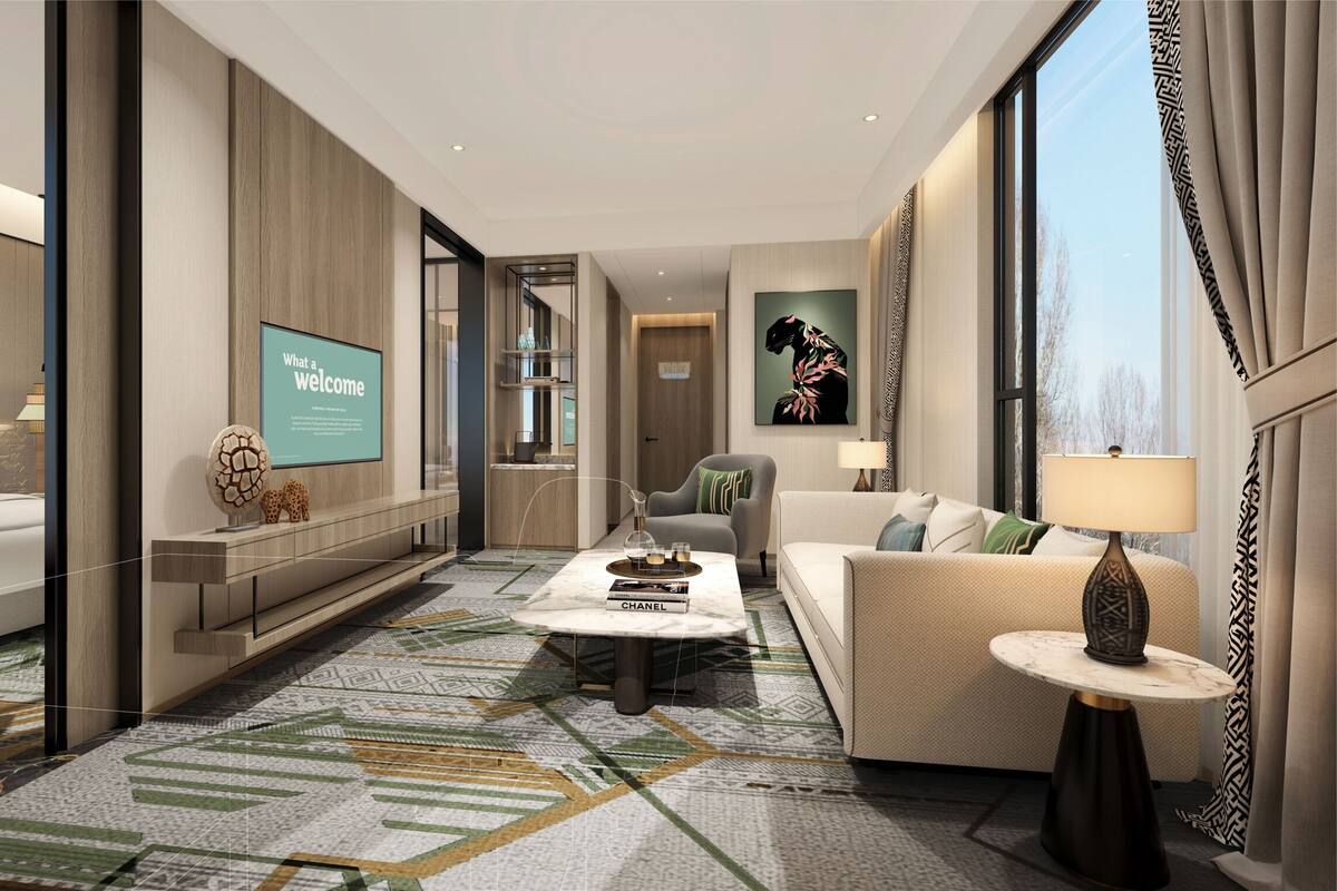 Une chambre d’hôtel moderne, dotée d’un grand lit, d’un canapé, d’une table basse et d’un téléviseur affichant le message : « Quelle belle attention ! »