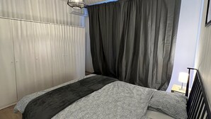 Ein Schlafzimmer mit Bett, einer Hängeleuchte, einem Fenster mit Vorhängen und einem Nachttisch.