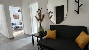 Ein modernes Wohnzimmer mit einem schwarzen Sofa, zwei gelben Kissen, einem runden Spiegel und einer Vase mit Trockenpflanzen.