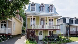 A two-story house with a balcony, a front porch, and a small garden area. - Free ferry | Aux Trois Filles (Lévis)