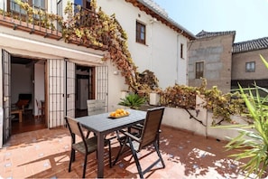 Eine Terrasse mit Tisch und Stühlen, ein weißes Gebäude mit Balkon und eine Steinmauer.