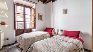 Ein Schlafzimmer mit zwei Betten, einem Fenster mit Holzläden, einer Wandlampe und einem gerahmten Bild.