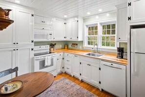 Una cocina con armarios blancos, encimera de madera, fregadero, estufa y ventana con vistas a zonas verdes.