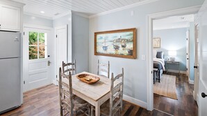 Un comedor con una mesa y sillas de madera, un cuadro en la pared y vistas al exterior a través de una puerta.