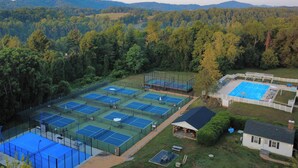 Vista aérea de un complejo de tenis con varias canchas, rodeado de bosque denso y colinas.