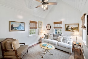 A living room with a sofa, armchair, coffee table, and a ceiling fan.
