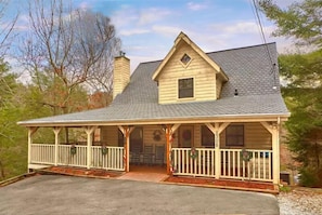 Une maison en bois à deux étages, avec un toit à pignon, une véranda dotée de balustrades blanches et une cheminée.