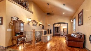 Amplia sala de estar con piso de madera, un sofá de cuero, un mueble de madera y una escalera con una rueda decorativa.