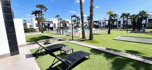 Ein moderner Poolbereich im Freien mit Liegestühlen, Palmen und blauem Himmel.