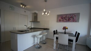 A modern kitchen with a central island, white bar stools, a dining table with chairs, and a pendant light. - Groundfloor Varudi Aguas Nuevas, Torrevieja (Torrevieja)