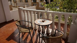 A balcony with two wicker chairs and a small round table, white balustrades, and a potted plant.