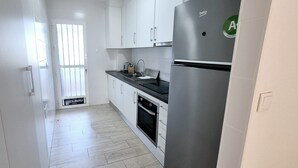 A modern kitchen with white cabinets, a stainless steel refrigerator, and a wooden floor.