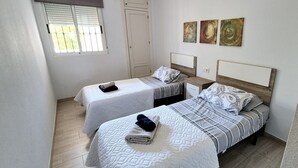 A bedroom with two beds, a window with blinds, and three wall-mounted artworks.