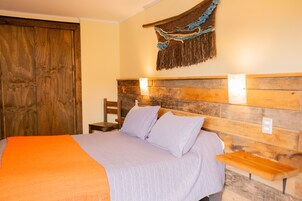 Un dormitorio con cabecera de madera, cama con manta naranja y un tapiz colgado en la pared.