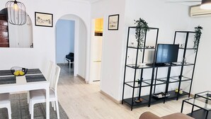 Een moderne woonkamer met een eethoek, een televisie op een zwarte kast en een bruine bank.