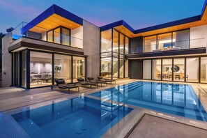 A modern house with a swimming pool, glass doors, and a dining area.