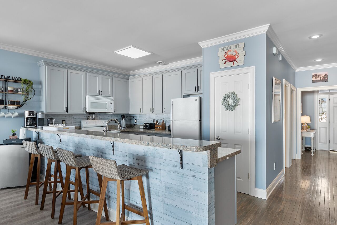 A kitchen with a central island, bar stools, white cabinets, and a microwave.