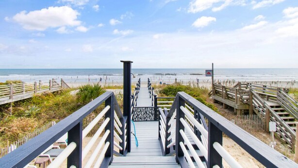 A wooden boardwalk leading to a beach with a clear sky.
