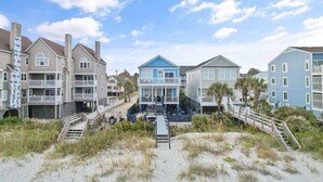 A beachfront property with multiple-story buildings, a sandy beach in the foreground, and a clear sky.