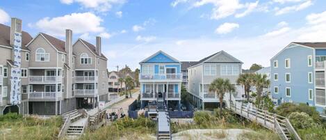A beachfront property with multiple-story buildings, a sandy beach in the foreground, and a clear sky.