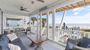 A covered outdoor area with a wooden table, sofas, and a view of the beach.