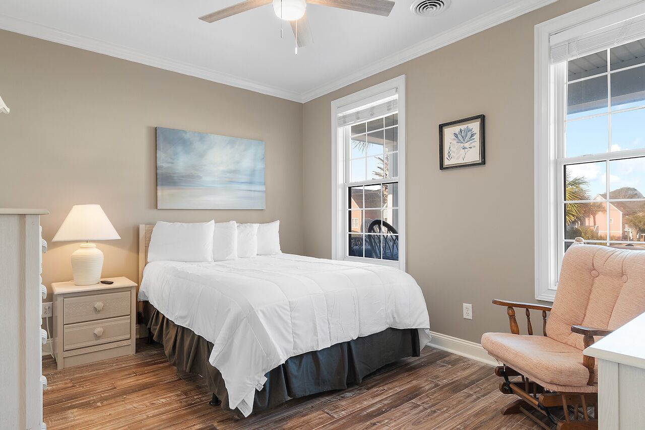 A bedroom with a bed, nightstand, chair, and artwork on the wall.