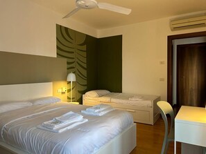 A hotel room with two beds, a desk, a chair, a ceiling fan, and an air conditioning unit.