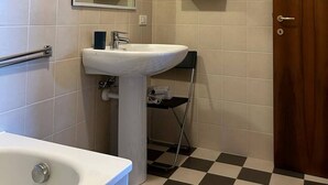 Ett badrum med ett vitt handfat, en spegel, en dusch och en dörr.