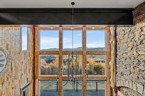 A room with a large window, a chandelier, and a stone wall.