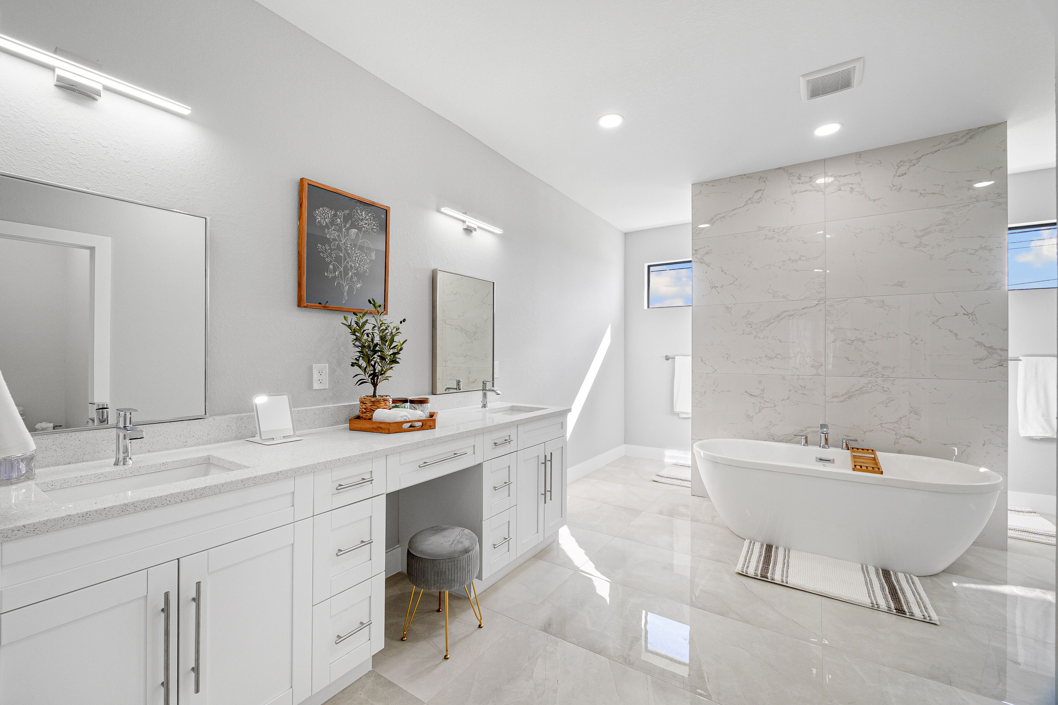 A modern bathroom with a freestanding bathtub, a large vanity with a mirror, and a potted plant.