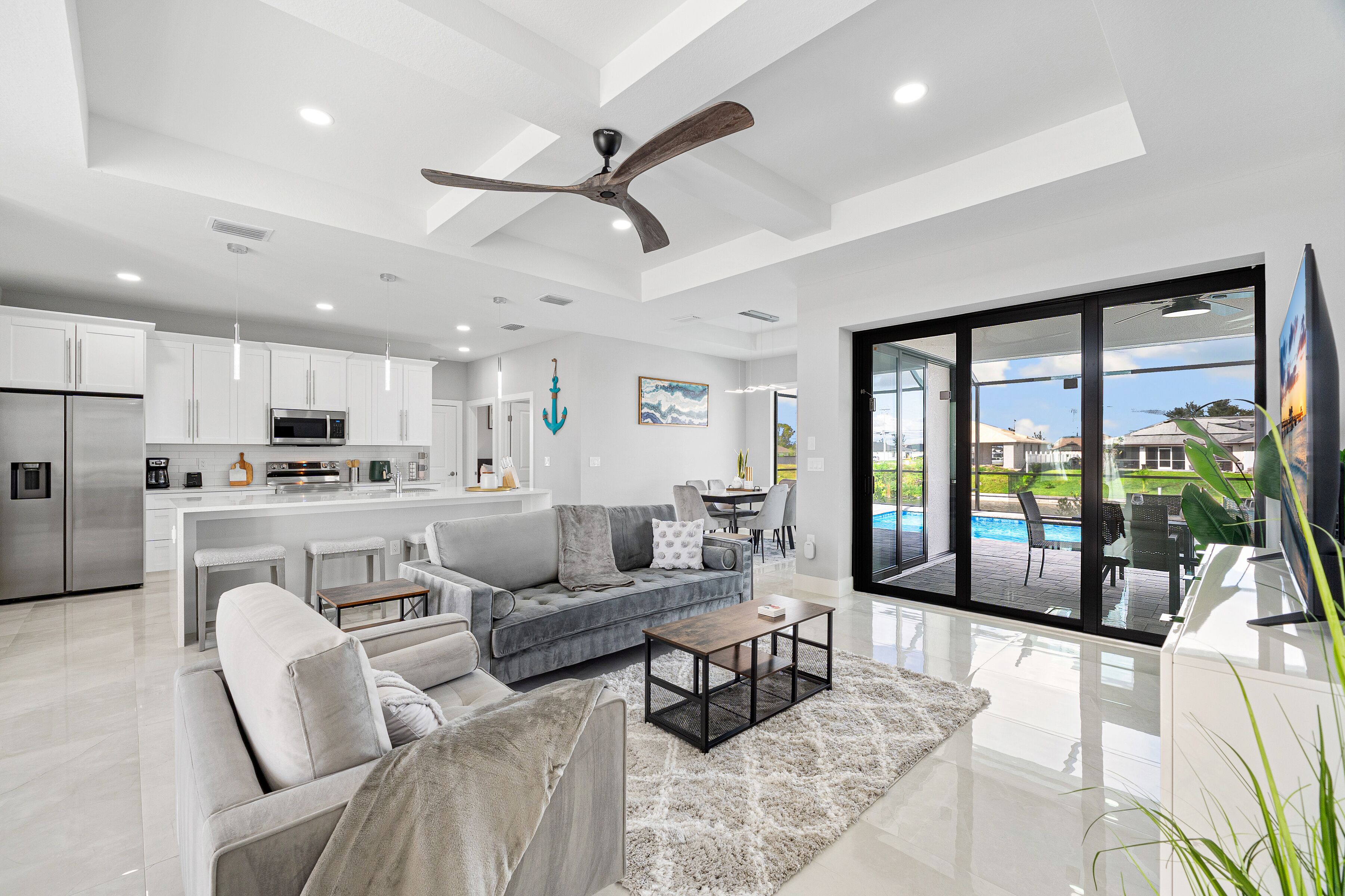 A modern living room with a grey sofa, a coffee table, and a view of a swimming pool through large glass doors.