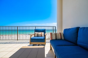 A balcony with a view of the beach, a blue chair, and a blue sofa.