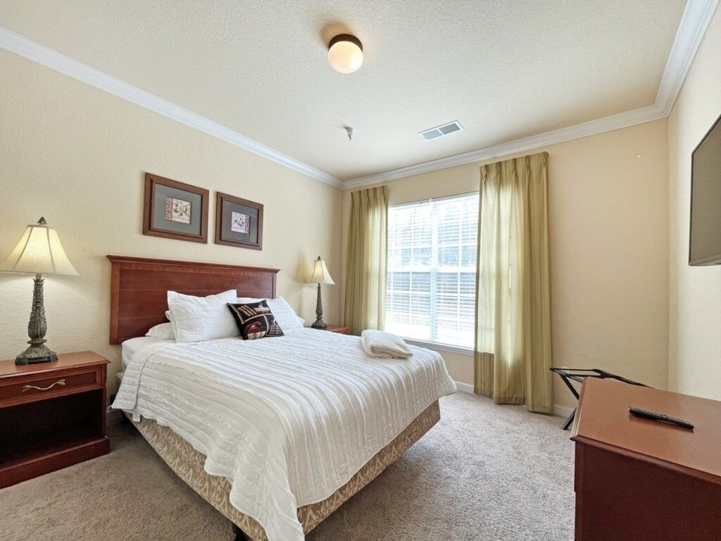 A hotel room with a large bed, two bedside lamps, a desk, and a window with curtains.