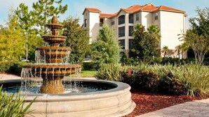 Una fuente de varios niveles en un jardín ajardinado, con un edificio al fondo.
