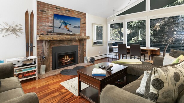 A living room with a fireplace, a dining area, and large windows.