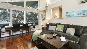 A modern living room with a dark grey sofa, a wooden coffee table, and a dining area with a wooden table and chairs.