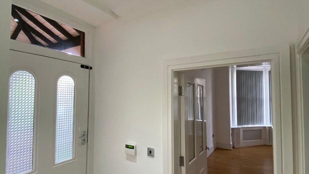 Un couloir aux murs blancs, doté d’un plancher en bois et d’une porte avec une fenêtre.